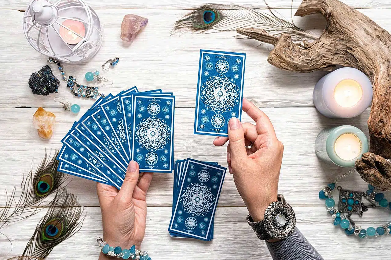 Fortune teller woman with blue tarot cards over white wooden table background.